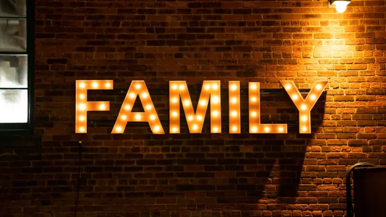 Šviečiantis užrašas „FAMILY“ ant raudonų plytų sienos jaukioje vakaro atmosferoje.