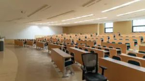 Tuščia moderni universiteto auditorija Klaipėdoje su mediniais suolais ir kėdėmis.