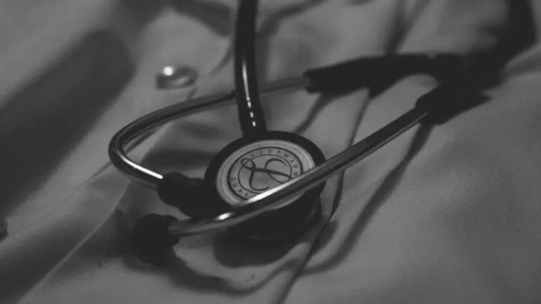 Juodai baltas stetoskopas, gulintis ant mediko chalato, simbolizuojantis medicinos profesijos pažinimą.