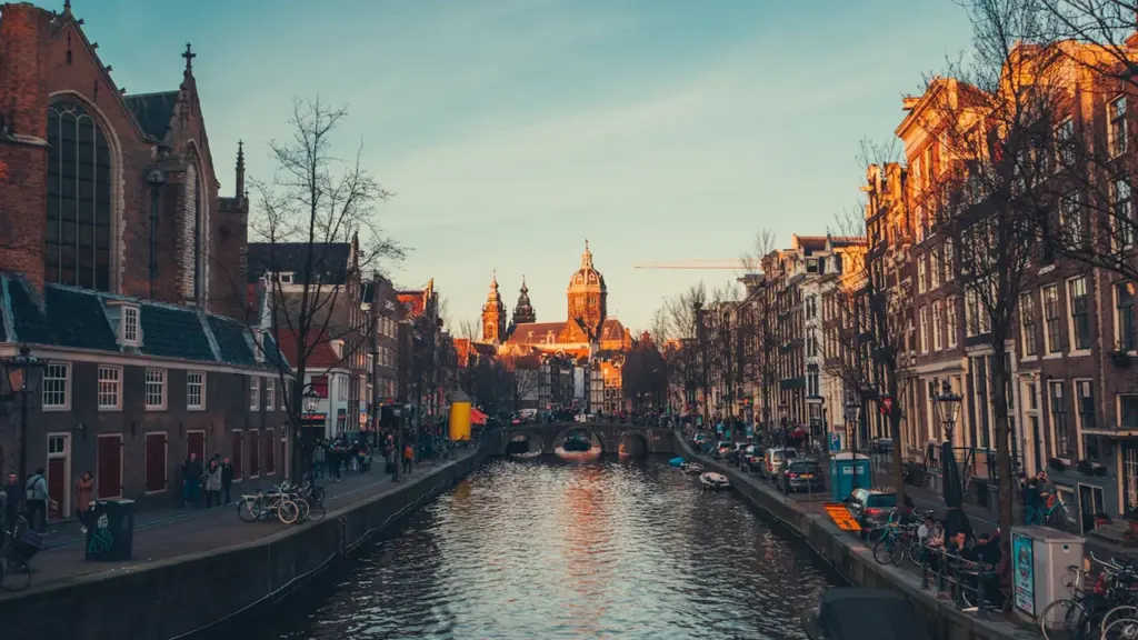 Vaizdingas Amsterdamo kanalas su istoriniais pastatais ir prišvartuotomis valtimis saulėlydžio metu