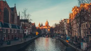 Vaizdingas Amsterdamo kanalas su istoriniais pastatais ir prišvartuotomis valtimis saulėlydžio metu