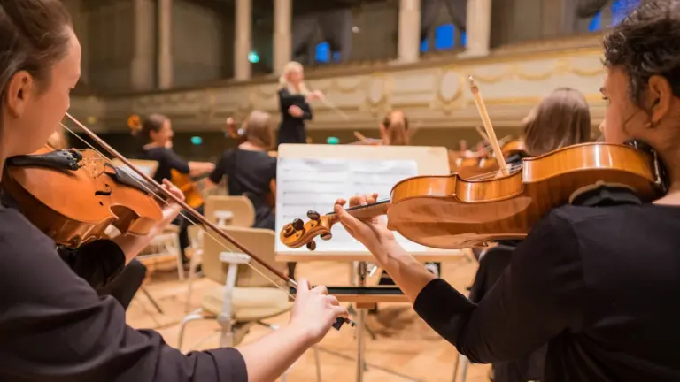 Klasikinės muzikos atlikėjai groja smuikais orkestro repeticijoje arba koncerte