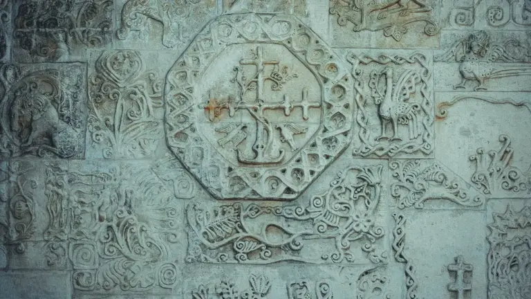 Detalus senovinis akmens raižinys su kryžiumi ir mitologinėmis figūromis ant sienos.