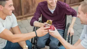 Besišypsantys jauni vyrai, įskaitant neįgaliojo vežimėlyje sėdintį studentą, bendraujantys prie stalo.
