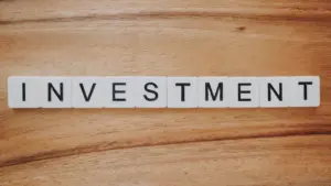 Žodis „INVESTMENT“ sudėliotas iš plastikinių raidžių ant medinio paviršiaus, simbolizuojantis finansų temą.