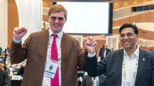 Du besišypsantys vyrai su akiniams laiko vienas kitą už rankų konferencijos salėje.