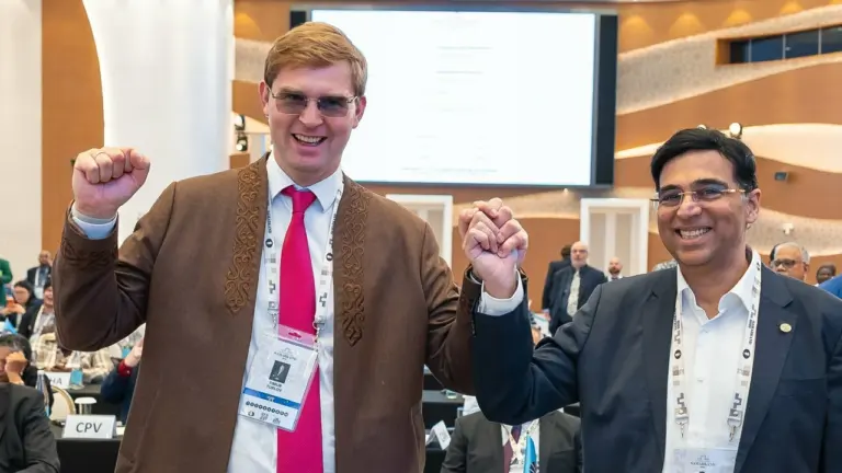 Du besišypsantys vyrai su akiniams laiko vienas kitą už rankų konferencijos salėje.