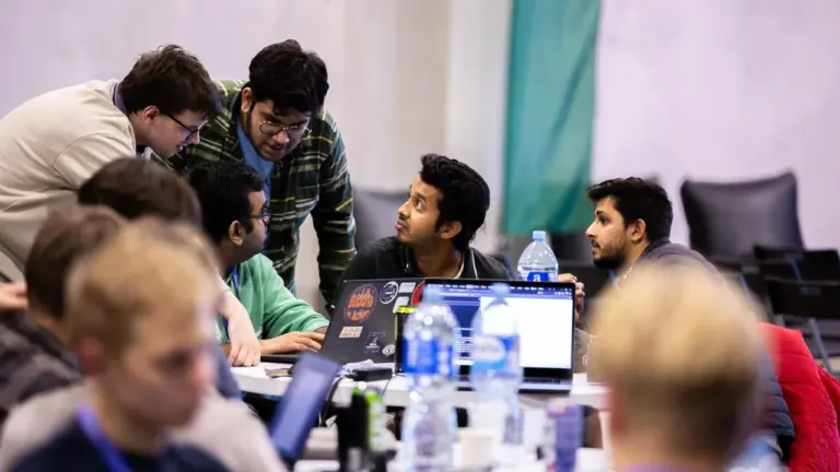Grupė studentų susibūrę aplink nešiojamąjį kompiuterį ir intensyviai diskutuoja apie atliekamą technologinę užduotį.