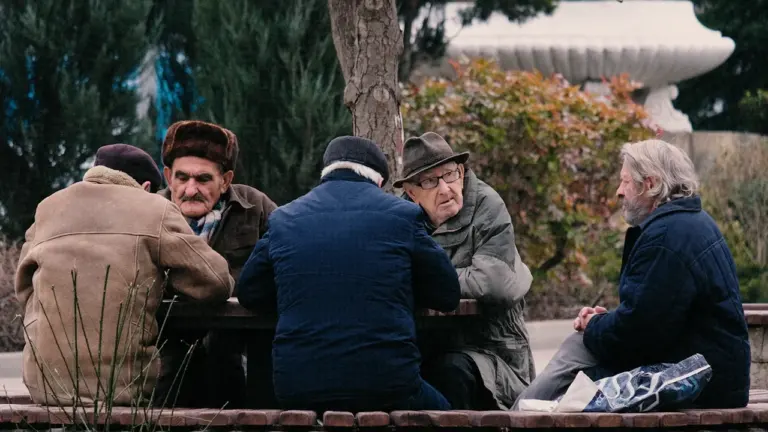 Pagyvenę vyrai susėdę prie stalo parke bendrauja ir leidžia laisvą laiką lauke.