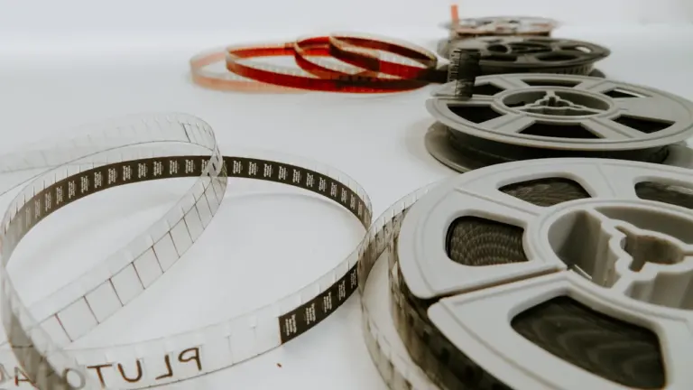 Keli 8mm kino juostos ritiniai išdėlioti ant balto stalo renginiui paminėti.